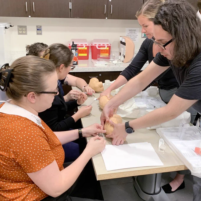Three interns practice spinal taps on infant simulation manikins as two instructors assist.