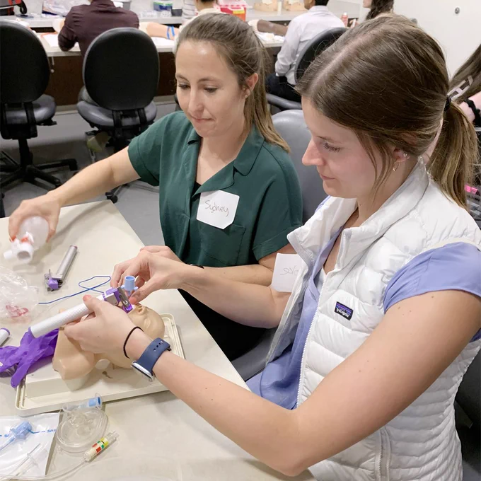 Two interns practice airway support procedures on an infant simulation manikin task-trainer.