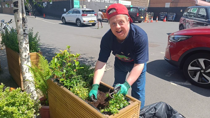 A Share student using a hand hoe to do some weeding in a wooden planter.
