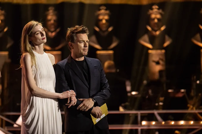Elizabeth Debicki and Ewan McGregor present onstage at the Olivier Awards. Elizabeth wears a long white dress with blonde hair and Ewan wears a dark suit with short dark hair.