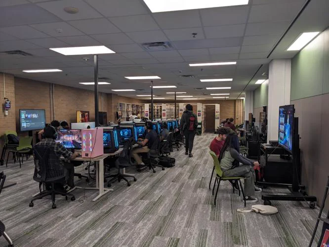 A photo of the commons of the media library with many students sitting at the console and computer stations.