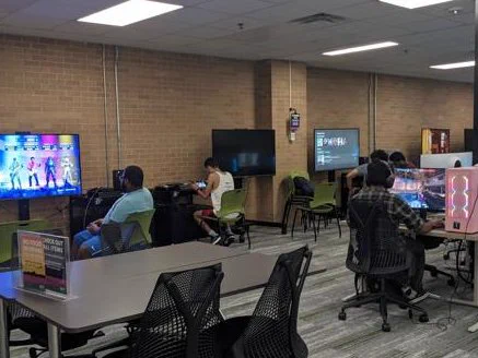 A photo of the commons of the media library with many students sitting at the console and computer stations.