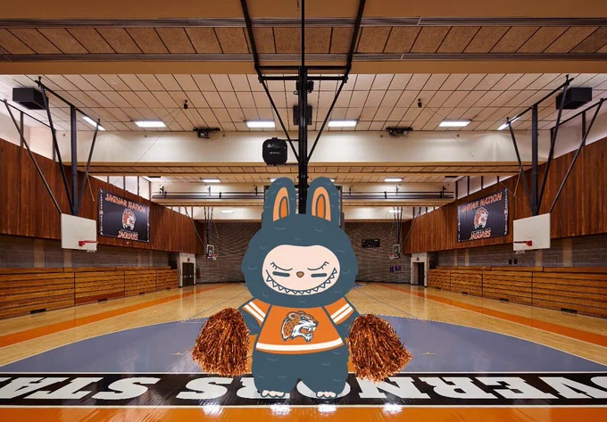 Illustration of a Governors State University's Labubu doll standing at center court in a gymnasium with wooden bleachers and a basketball court. Banners displaying 'Nationals Basketball' hang in the background.