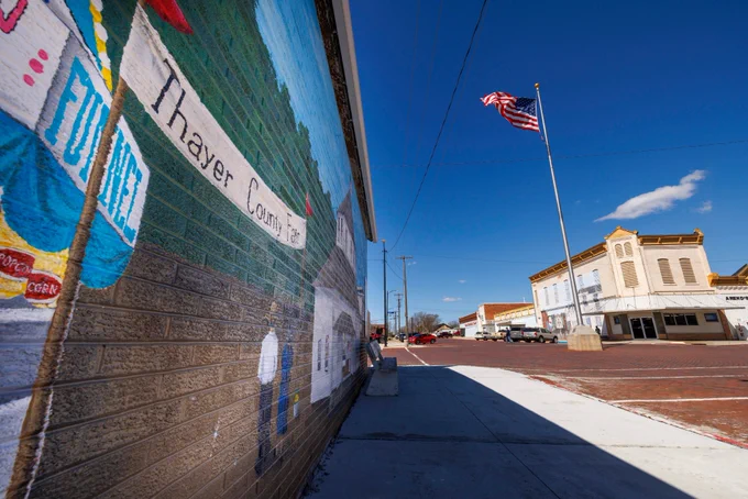 A Thayer County mural is painted on a brick wall in downtown Deshler, Nebraska. An American flag flies in the background. (Craig Chandler/University Communication and Marketing)