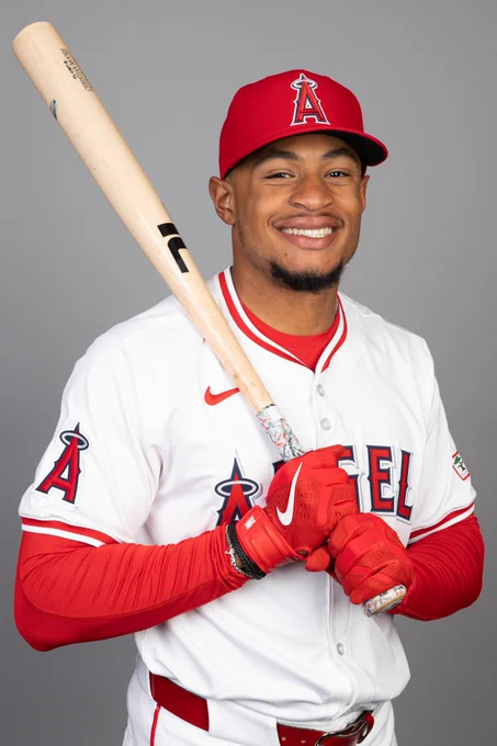 Christian Moore smiles while holding his bat over his right shoulder. He wears a red Los Angeles Angels hat and white uniform top.