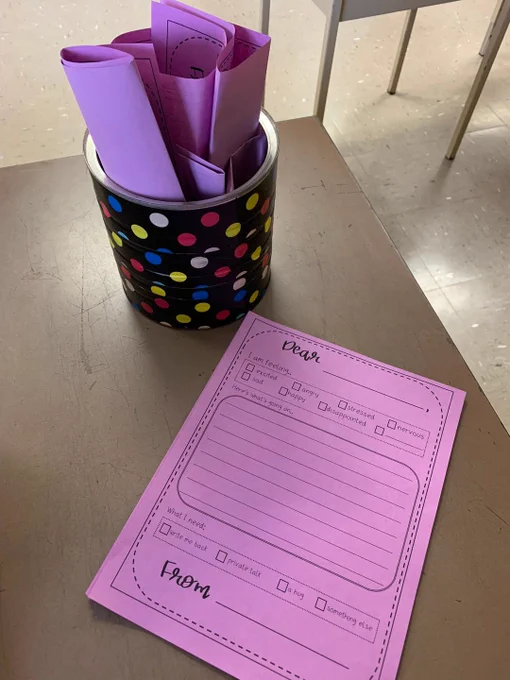 Container with pink rolled-up sheets of paper. Beside the container is an example of "Teacher Mail," which offers a form for students to complete with their feelings and worries.