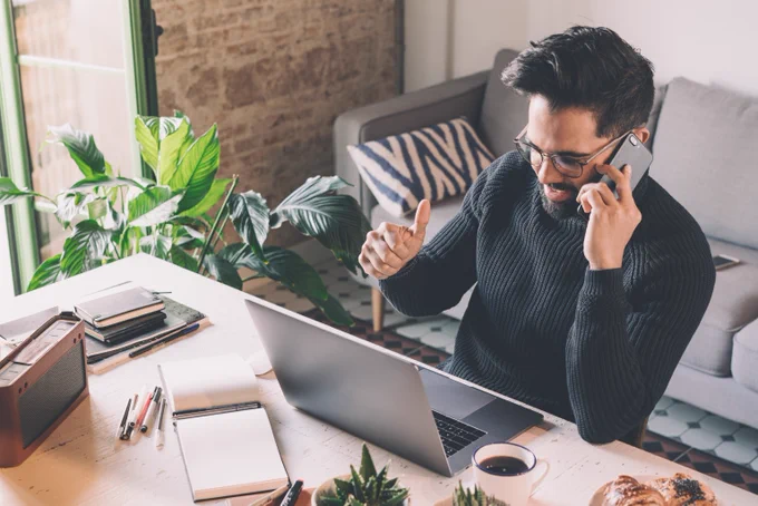 Male working from home using mobile whilst looking at laptop.