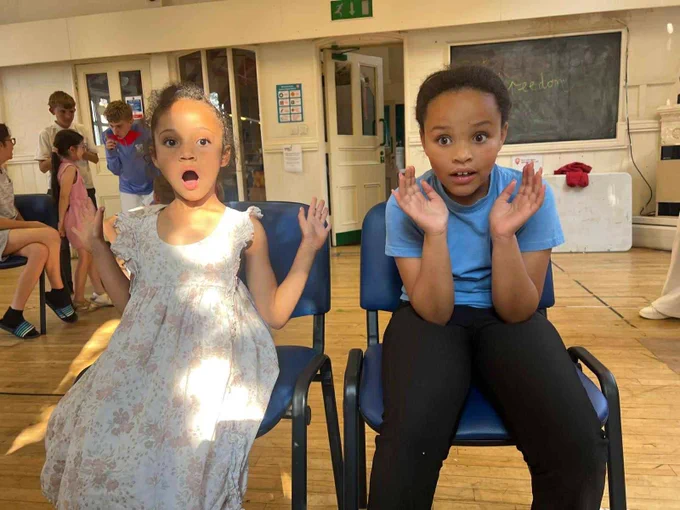 Two young people sitting in chairs making shocked faces