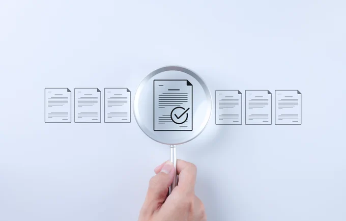White background with a horizontal row of symbols representing documents.  A hand holds a magnifying glass over one of the symbols, which shows a tick in a circle.
