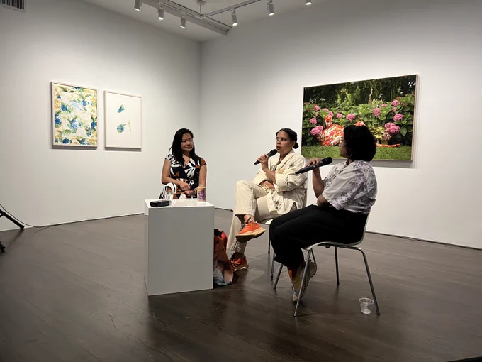 Three people on a panel discussion in a white-walled art gallery.

