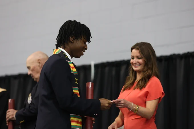 A graduating student is smiling while receiving a diploma.