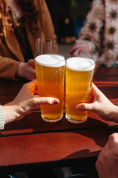 Two full pints held together in a cheers on a brown picnic table.