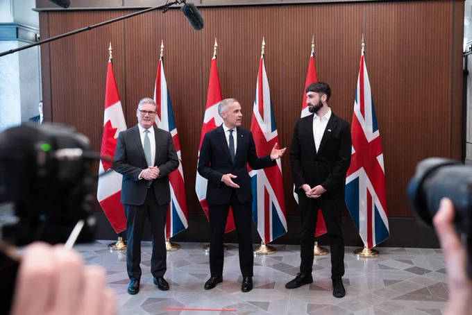 Prime Minister Mark Carney, Prime Minister Keir Starmer, and CEO of technology company Cohere, Aidan Gomez, stand in front of an array of Canadian and UK flags.