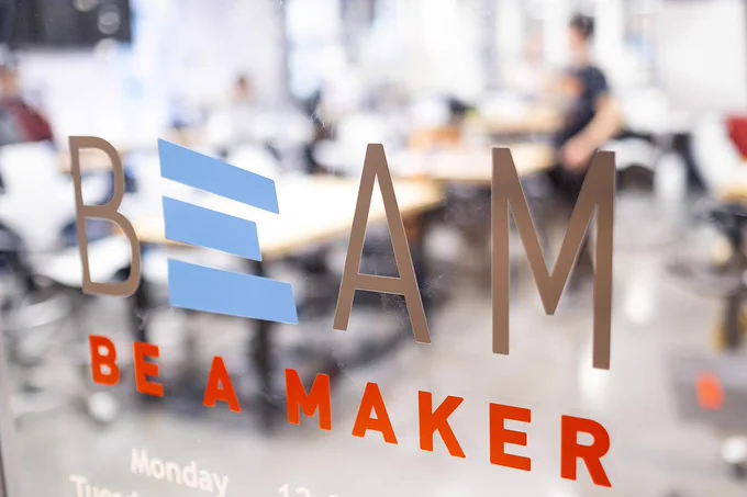 The BeAM logo on a window on UNC's makerspace says "Be a Maker"