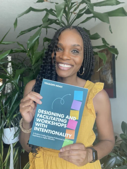 A young Black woman smiling at the camera, holding a copy of her new book, Designing and Facilitating Workshops with Intentionality.