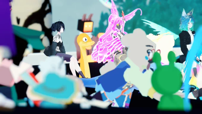 A group of VRChat players is seated and facing forward, watching a panel. Visible avatars include a glowing pink character with large wings and long hair, a bright yellow snake-like avatar with a smiling face, a humanoid with short black hair and a black outfit, a teal-haired cat-eared avatar with a black jacket, a green frog-like character, a bear-like character in a blue outfit, and several others in pastel and vibrant colors. The setting appears lively and full of varied avatar designs.