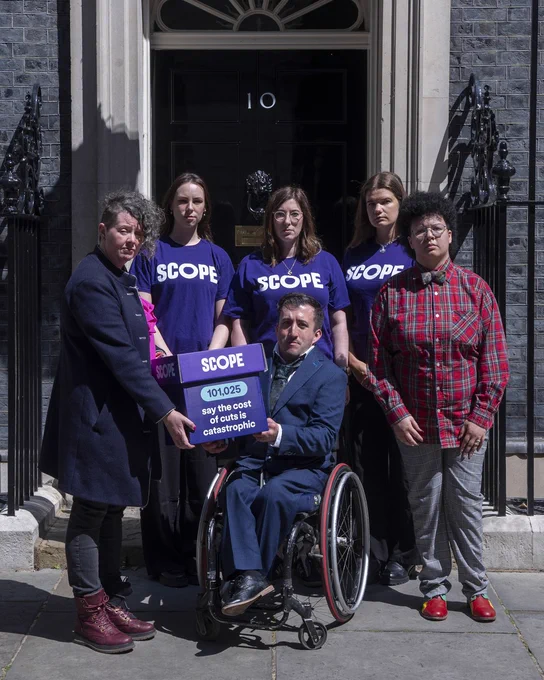 6 people in front of 10 Downing Street. 3 are wearing Scope t-shirts. The other 3 are in front. 2 of them, one a wheelchair user, are holding a purple box that reads, '101,025 say the cost of cuts is catastrophic' with the Scope logo on the lid.