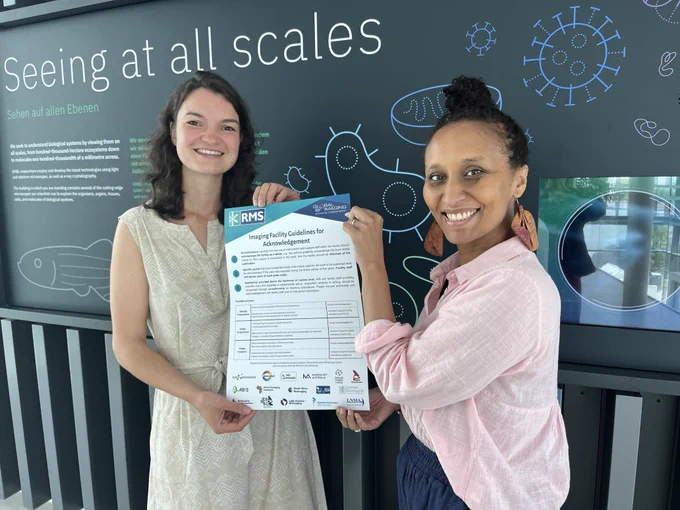 Two smiling staff members at an imaging facility hold up the 'Acknowledgement Guidelines' poster