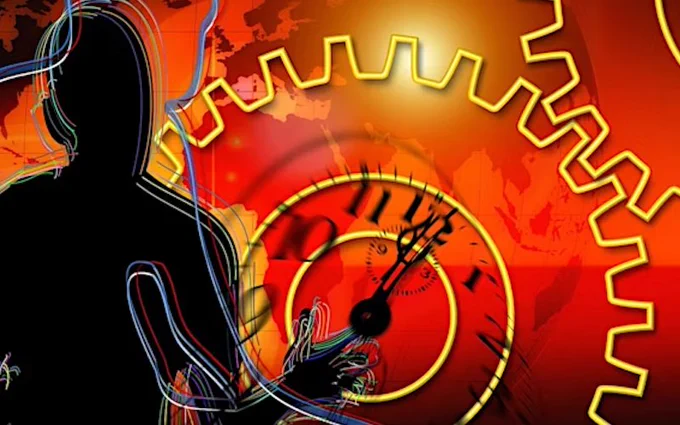 An abstract image showing a black silhouette of a person on the left, and a large clock that is also part of two big yellow cogs in the background. This part of the image is red, yellow and orange, and behind there is an outline of the map of the world.