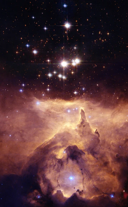 A group of white and blue stars sparkles in the darkness of space. In the background are orange galaxies, sprinkled all over. Below the stars, orange and yellow clouds of gas glow, revealing structures that look like rock formations and arches. Credit: NASA, ESA, and Jesús Maíz Apellániz (Instituto de Astrofísica de Andalucía, Spain); Acknowledgment: Davide De Martin (ESA/Hubble)