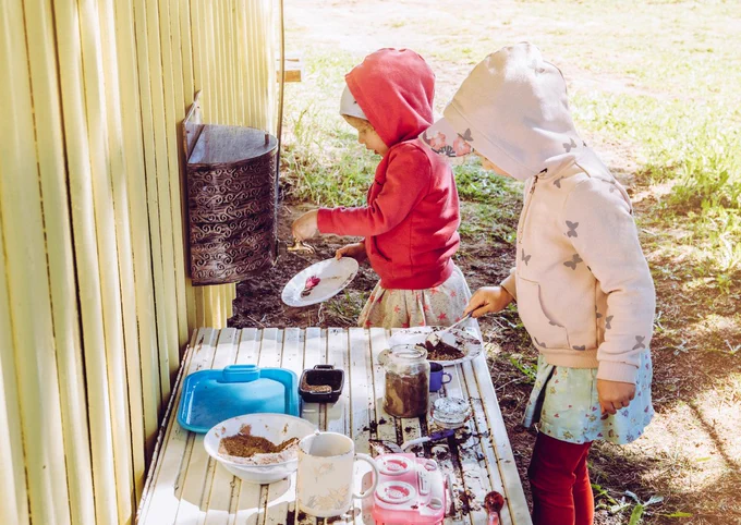 Photo of two young children playing in an outdoor mud kitchen