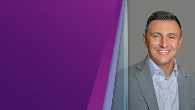 A front-facing headshot of Eric Moore smiling in front of a gray background, positioned next to a purple gradient