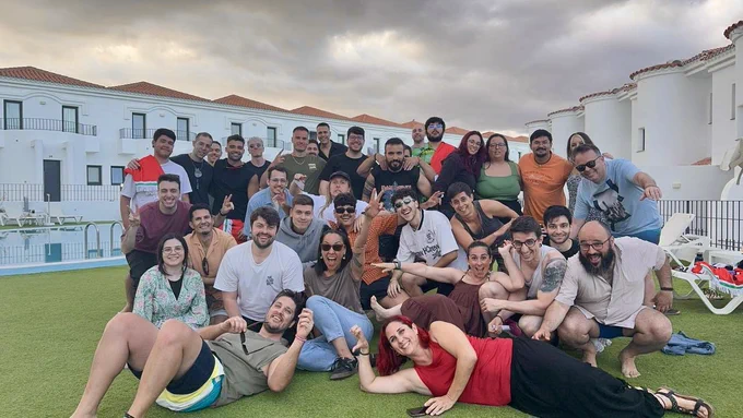 En esta foto está el mismo grupo que en la foto anterior, pero esta vez, en una pose más alocada y divertida. Algunas personas ríen a carcajadas, otras están tumbadas en el suelo o apoyadas en quienes tienen al lado. 