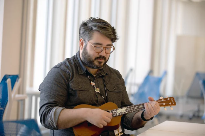 [ID: Pictured is a photo of a UTA Libraries staff member playing the ukulele.]