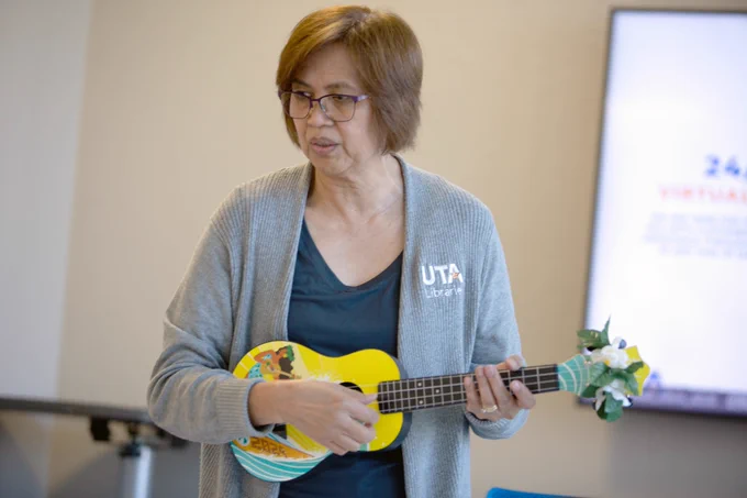 [ID: Pictured is a photo of a UTA Libraries staff member playing the ukulele.]