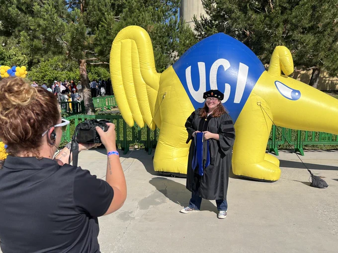 A graduate posing by Peter the Anteater