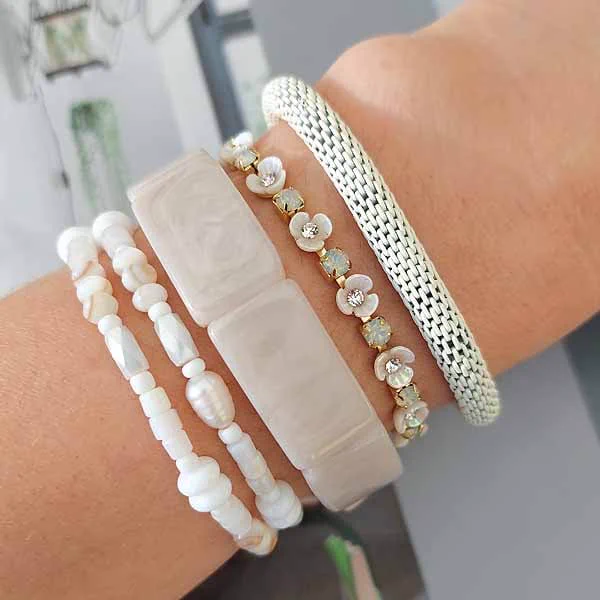 Close-up van een witte Biba armbandenset met resin, metalen details en bloemetjes, gestyled op een pols in zomers daglicht.