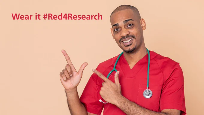 A man wearing red medical scrubs and a stethoscope points his fingers in the air. Above his hands text reads 'Wear it #Red4Research'.