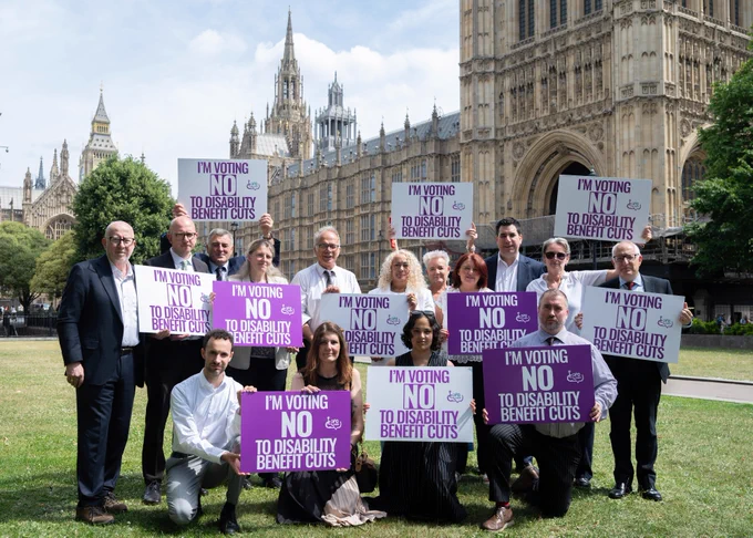 Image of 15 MPs outside Parliament holding DPO Forum placards that say 'I'm voting NO to disability benefit cuts'