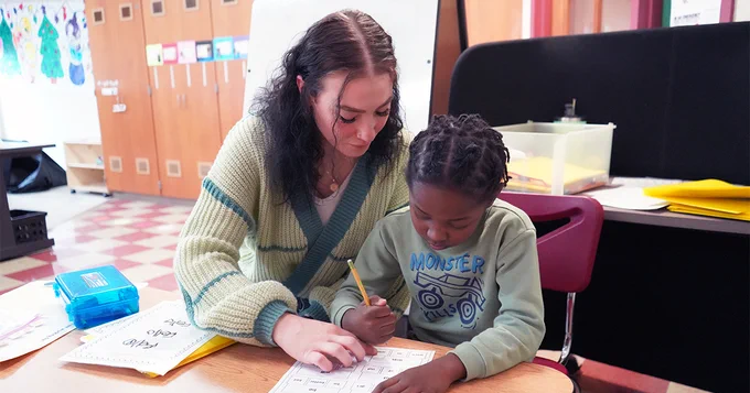 Photo of female graduate student working with elementary student in classroom