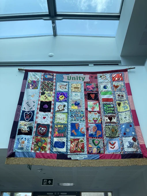 A colourful hanging quilt. The word 'unity' has been stitched at the top of it. 