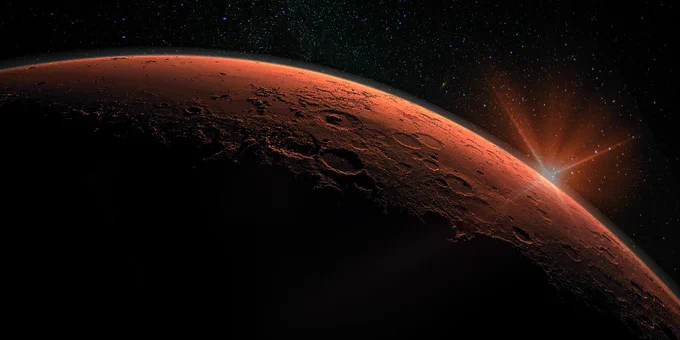 A striking image of planet Mars with a sunburst visible beyond its horizon, set against a starry space background.