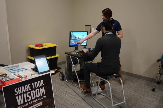 DOA LTE Communications Specialist taking a motorcycle simulation course alongside instructor at the Safety Open House event at Hill Farms State Office building.