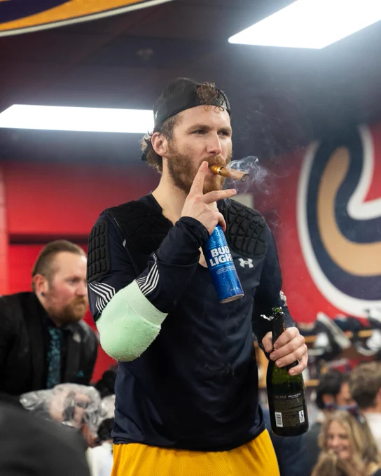 Matthew Tkachuk smoking a cigar while holding a beer and champagne in the locker room.