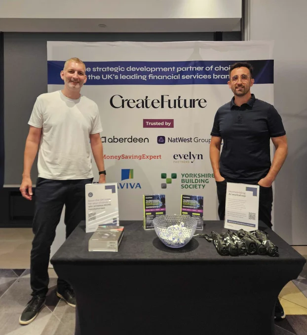 Two men standing in front of an exhibition stand, with a banner displaying 'CreateFuture' as well as a table of posters and merchandise.