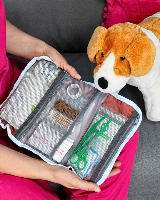 A stuffed toy Jack Russell dog sits next to an open pet first aid kit, showing the supplies that it holds.
