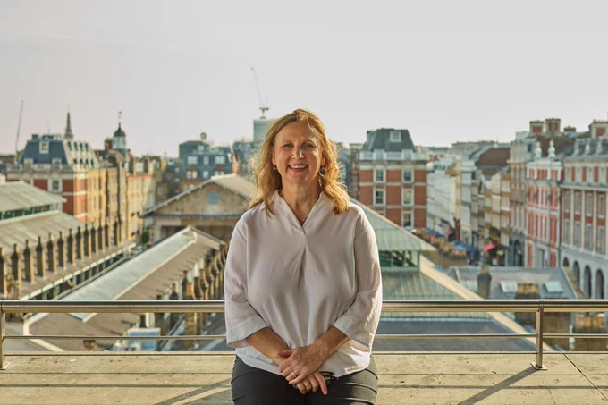 Angela Hartnett smiling at the camera, standing on a rooftop with a view of Covent Garden in the background.