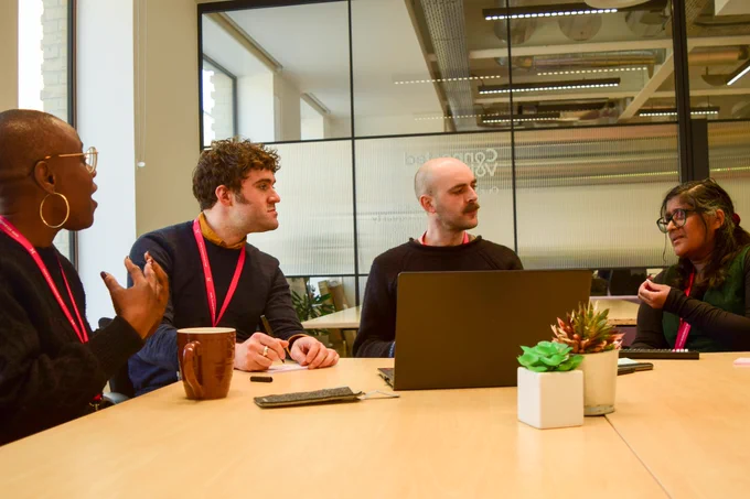 Four Connected Voice staff members gathering around a laptop in a meeting room at One Strawberry Lane