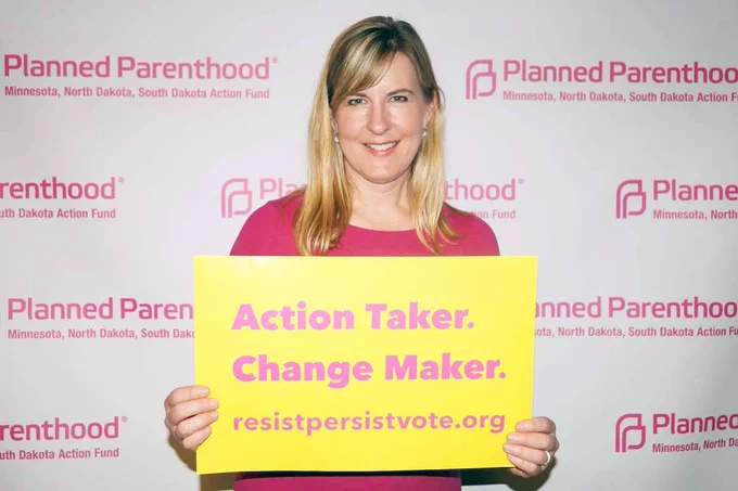 Speaker Emerita Melissa Hortman holding a sign that reads "Action Taker. Change Maker. resistpersistvote.org" at a Planned Parenthood event.
