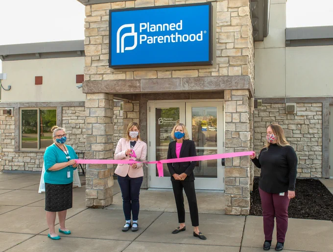 Two individuals holding a ribbon for a ribbon-cutting ceremony in front of a Planned Parenthood clinic with Speaker Emerita Melissa Hortman and former PPNCS CEO Sarah Stoesz