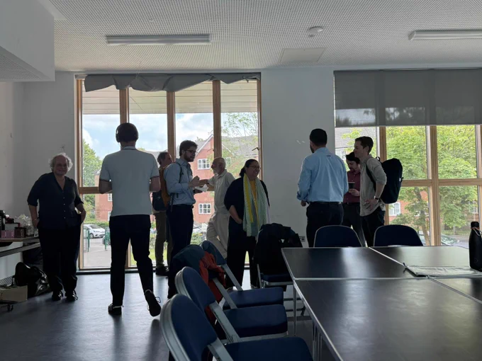 Attendees of various ages and ethnicities stood up socialising with one another at the meeting. 
