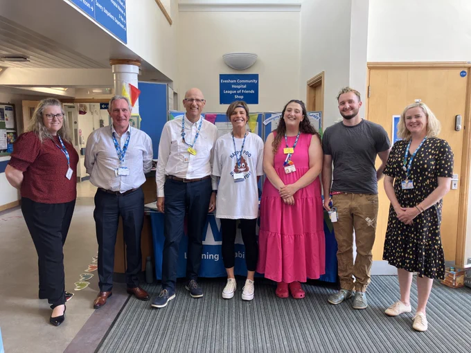 Staff members stand smiling in front of a blue table with “NHS Learning Disability Services” written on the cloth. Behind them is a display board with information on occupational therapy, psychology, and community nursing.