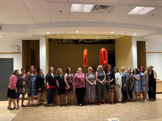 Group photo of the Ladies Auxiliary in attendance, with balloon numbers "60" behind them. 