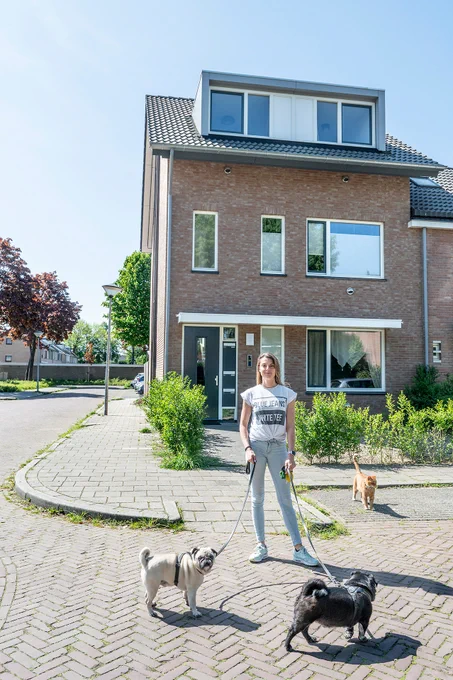 Jonge vrouw met 2 hondjes in een straat met huizen.
