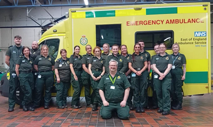 A group of people in green uniform stood in front of an ambulance.