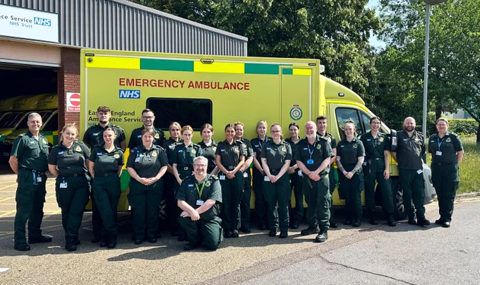 A group of people in green uniform stood in front of an ambulance.